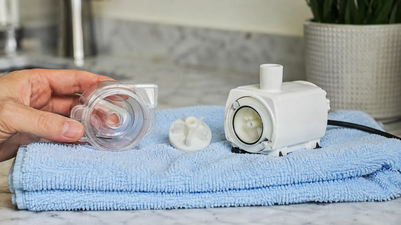 Tiny white fountain pump beside its little disassembled impeller housing on a light towel